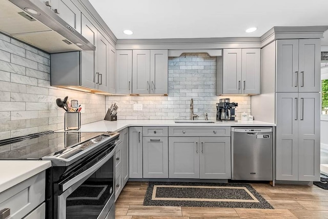 kitchen with stainless steel appliances, gray cabinets, a sink, under cabinet range hood, and light countertops