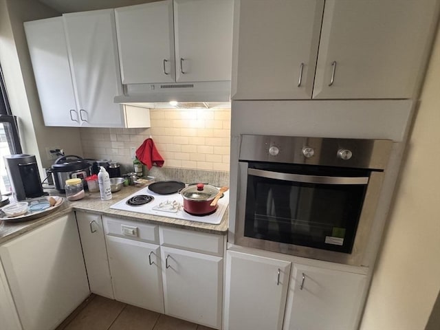 kitchen with backsplash, white electric stovetop, stainless steel oven, white cabinets, and light tile patterned flooring