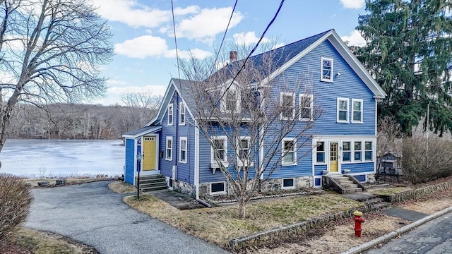 view of front of home with entry steps, aphalt driveway, roof with shingles, and a chimney