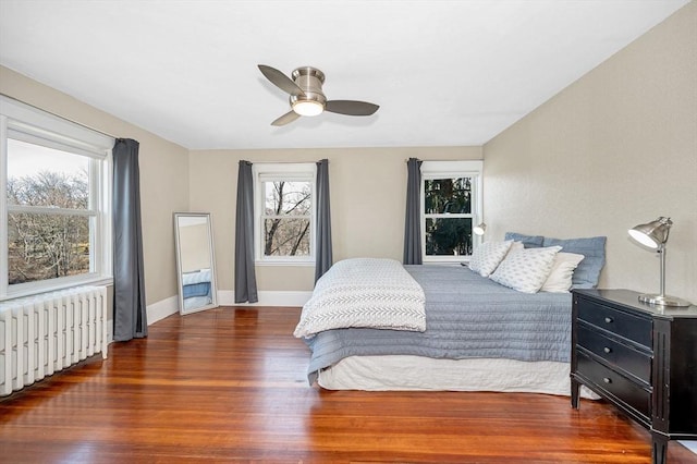 bedroom with multiple windows, radiator, baseboards, and wood finished floors