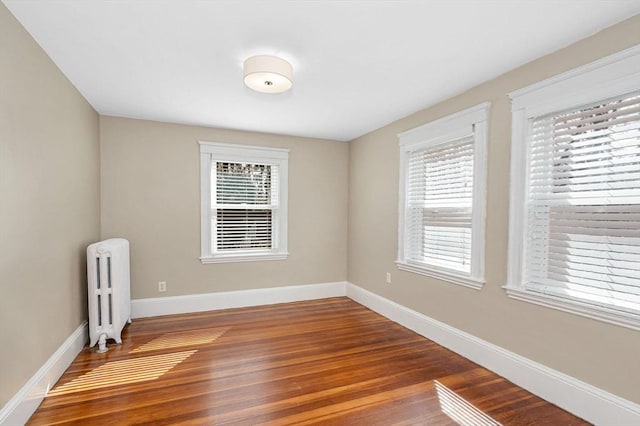 unfurnished room with radiator heating unit, wood finished floors, plenty of natural light, and baseboards