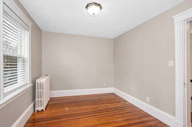 unfurnished room with baseboards, wood finished floors, and radiator heating unit