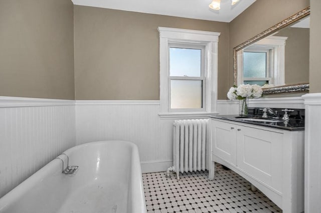 full bath with a freestanding bath, radiator heating unit, vanity, and wainscoting