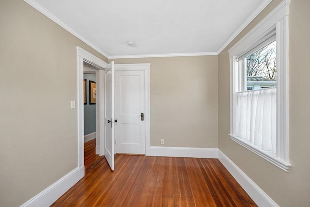 empty room featuring wood finished floors, baseboards, and ornamental molding