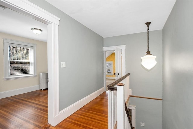 corridor with baseboards, an upstairs landing, wood finished floors, and radiator heating unit