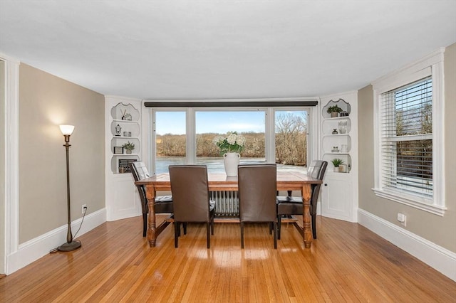 dining area with cooling unit, baseboards, and light wood finished floors