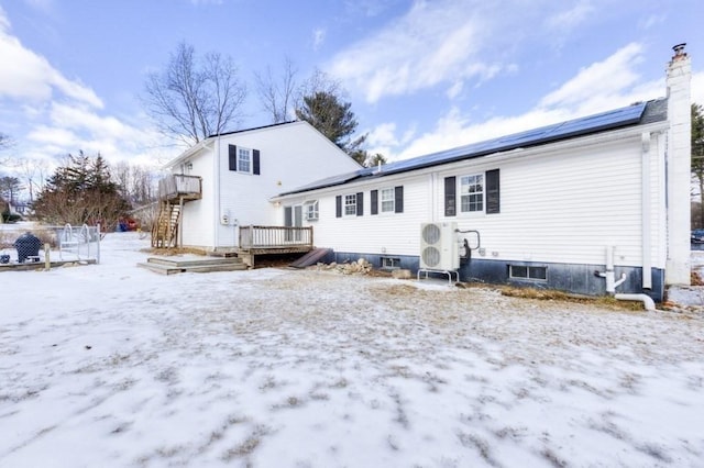 snow covered rear of property with a wooden deck, ac unit, and solar panels