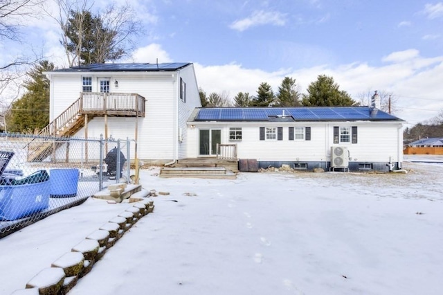 snow covered rear of property featuring a wooden deck and solar panels