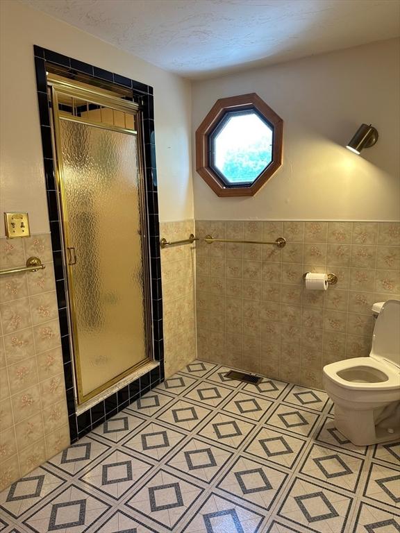 211 Stevens St, Marlborough, MA 01752 - bathroom featuring tile walls, a stall shower, toilet, a wainscoted wall, and tile patterned flooring
