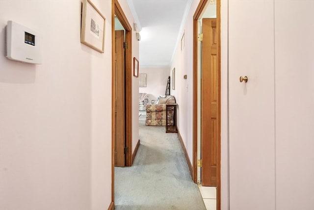 hall featuring crown molding, baseboards, and light carpet