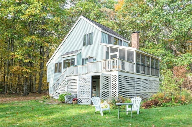 rear view of property featuring a wooden deck, stairs, a chimney, a yard, and a sunroom