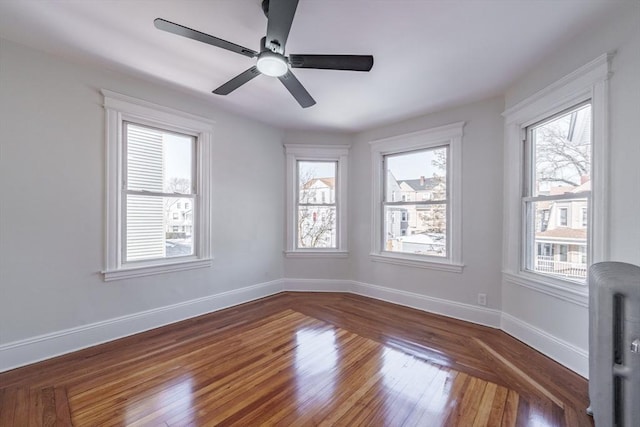 empty room featuring ceiling fan, plenty of natural light, and wood-type flooring