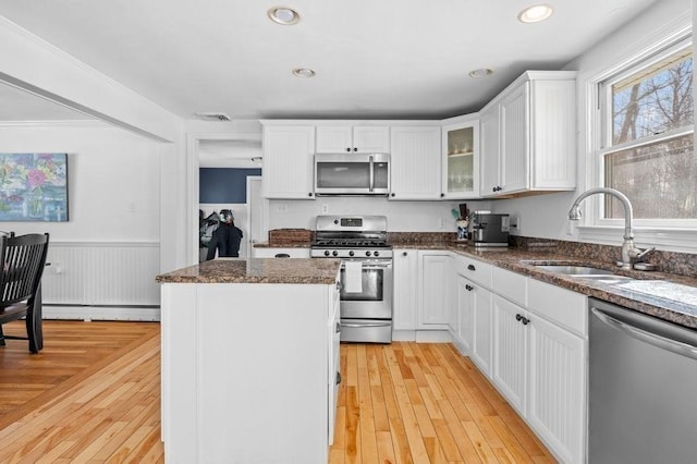 kitchen with sink, dark stone counters, white cabinets, stainless steel appliances, and a baseboard heating unit