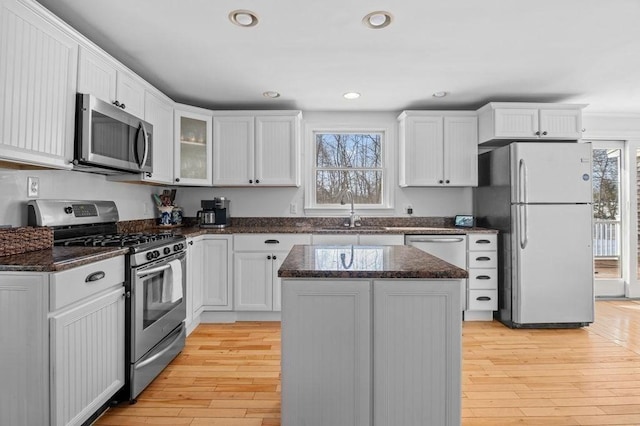 kitchen with sink, appliances with stainless steel finishes, white cabinetry, a kitchen island, and dark stone counters