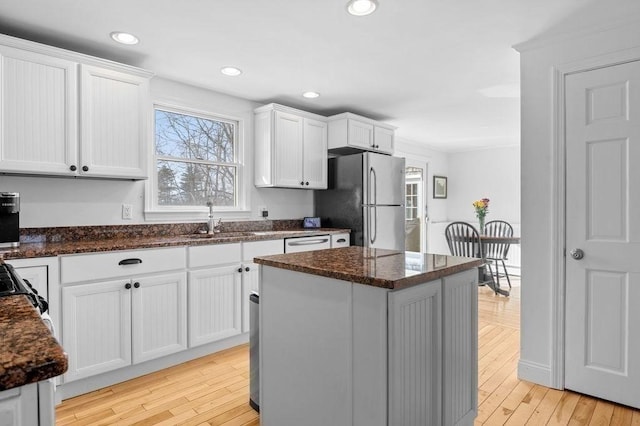 kitchen with stainless steel refrigerator, sink, white cabinets, a center island, and light hardwood / wood-style flooring