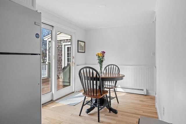 dining room featuring ornamental molding, a baseboard heating unit, and light hardwood / wood-style flooring