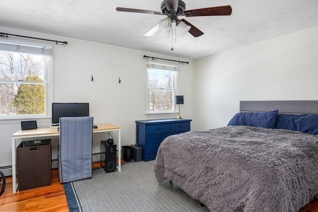 bedroom featuring a baseboard heating unit, hardwood / wood-style floors, and ceiling fan