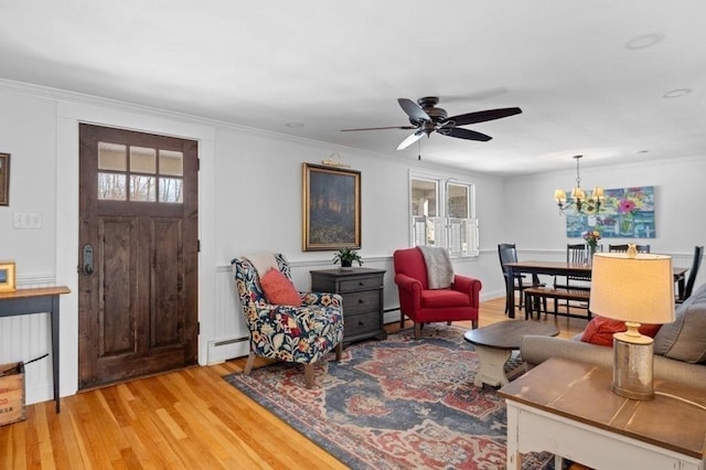 living room featuring hardwood / wood-style flooring, a baseboard radiator, ceiling fan with notable chandelier, and crown molding