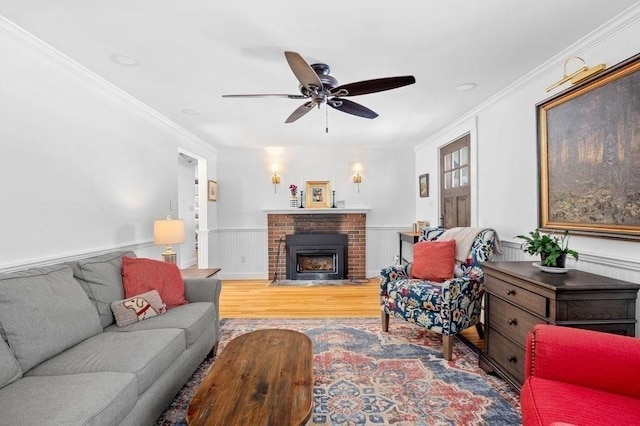 living room featuring ceiling fan, ornamental molding, a brick fireplace, and light hardwood / wood-style flooring