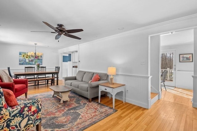 living room featuring ceiling fan with notable chandelier, ornamental molding, and light hardwood / wood-style floors