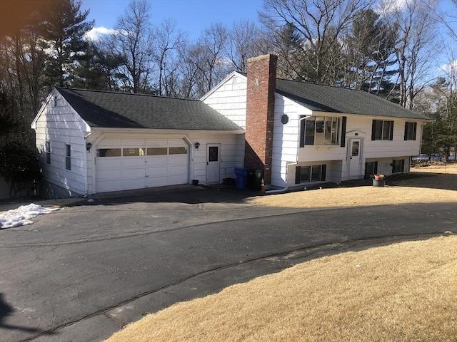 view of front of home with aphalt driveway, a chimney, an attached garage, and a shingled roof