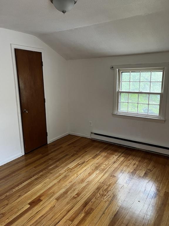 52-54 Campechi St, Springfield, MA 01104 - spare room featuring a baseboard radiator, light wood-type flooring, vaulted ceiling, and baseboards