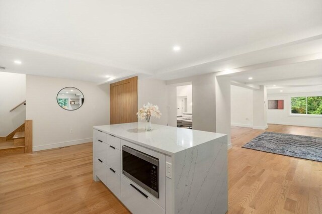 kitchen featuring a center island, white cabinets, stainless steel microwave, light hardwood / wood-style flooring, and light stone countertops