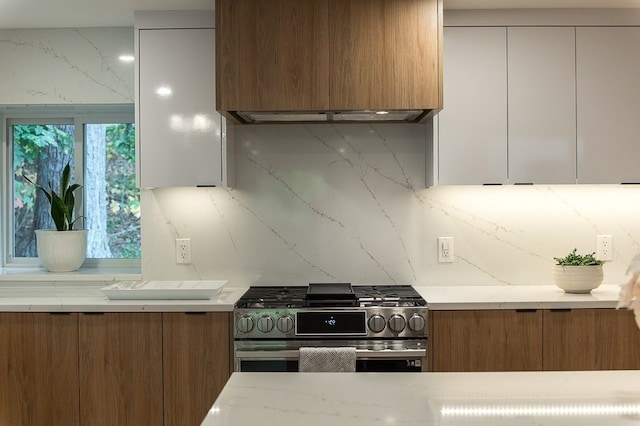 kitchen with backsplash, stainless steel gas stove, light stone counters, and white cabinets