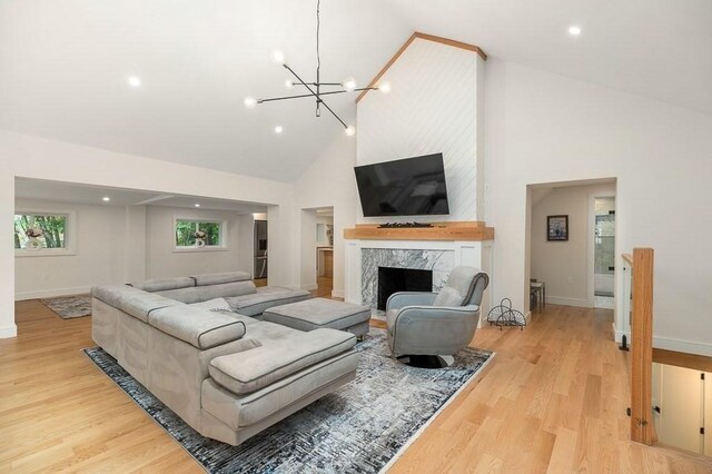 living room with high vaulted ceiling, light wood-type flooring, an inviting chandelier, and a fireplace