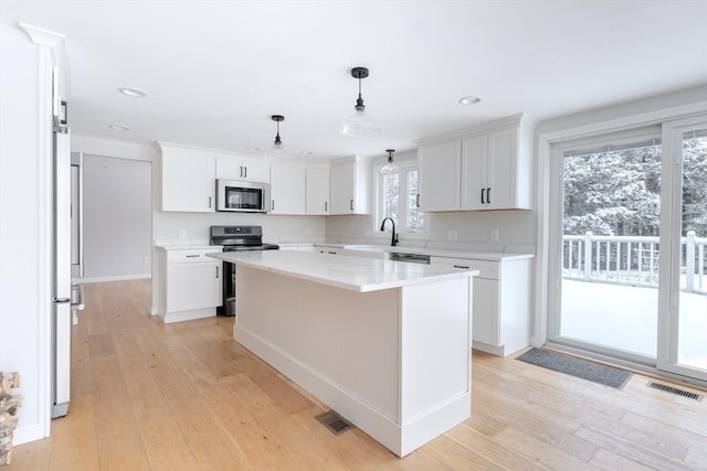 kitchen with stainless steel appliances, white cabinets, light hardwood / wood-style flooring, a kitchen island, and pendant lighting