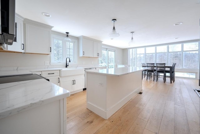 kitchen featuring light hardwood / wood-style floors, hanging light fixtures, a kitchen island, sink, and white cabinetry