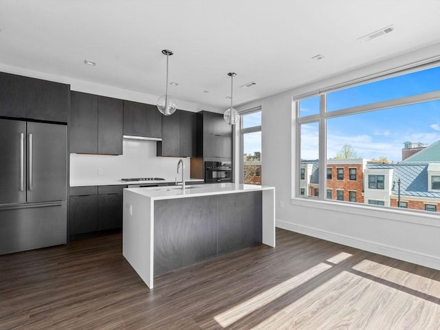 kitchen featuring gas cooktop, stainless steel fridge, light countertops, black oven, and a center island with sink