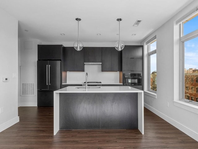 kitchen featuring oven, a sink, dark cabinets, high end refrigerator, and visible vents
