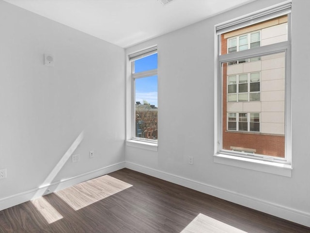 spare room with baseboards and dark wood-type flooring