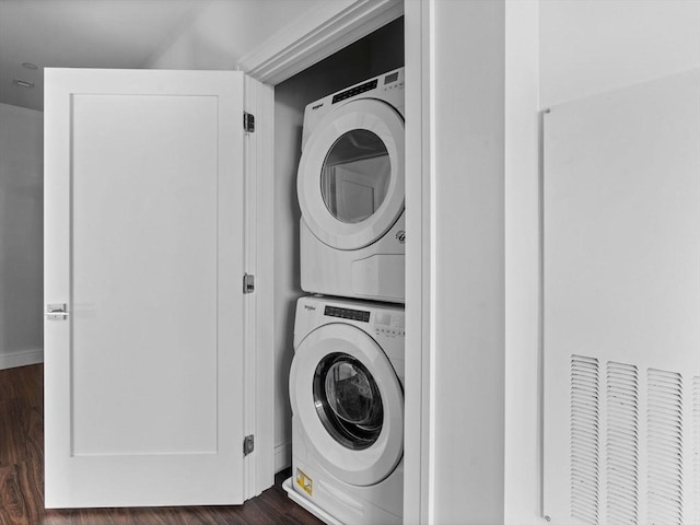 clothes washing area with stacked washer and clothes dryer, dark wood-style flooring, and laundry area
