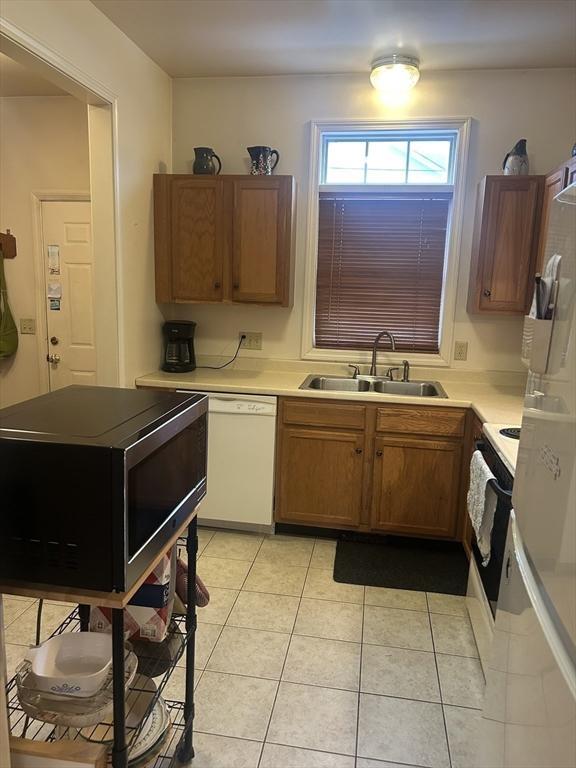 kitchen featuring brown cabinets, light tile patterned floors, light countertops, a sink, and white appliances