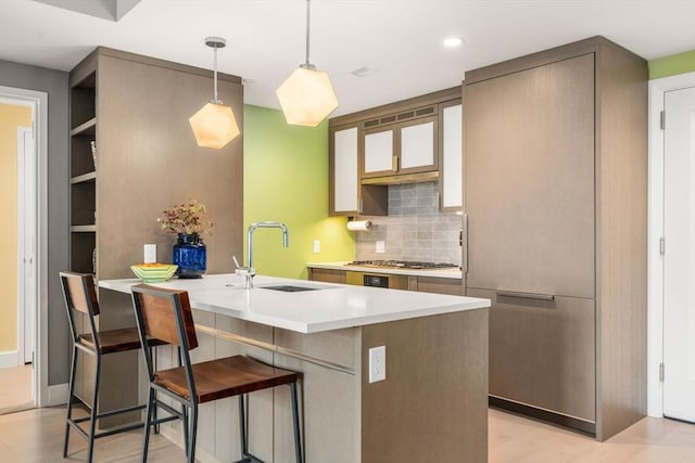 kitchen featuring a breakfast bar area, a peninsula, a sink, decorative backsplash, and light countertops