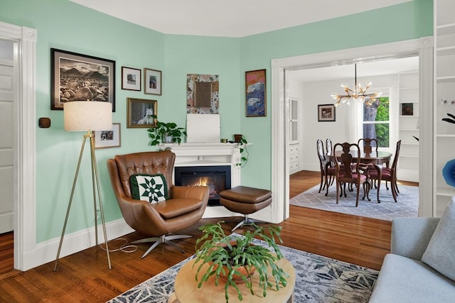 living area featuring a chandelier, wood finished floors, baseboards, and a glass covered fireplace