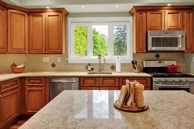 kitchen with appliances with stainless steel finishes, a sink, healthy amount of natural light, light stone counters, and recessed lighting