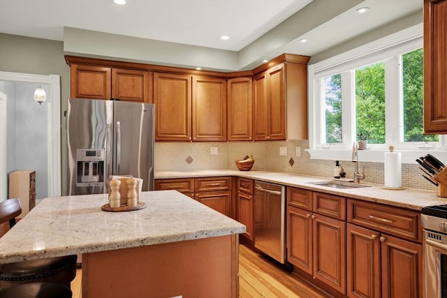 kitchen with stainless steel appliances, a sink, light stone counters, light wood-style flooring, and brown cabinetry