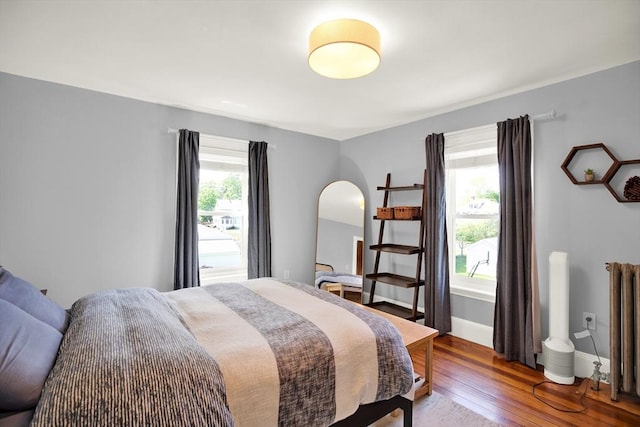 bedroom with radiator heating unit, arched walkways, hardwood / wood-style floors, and baseboards