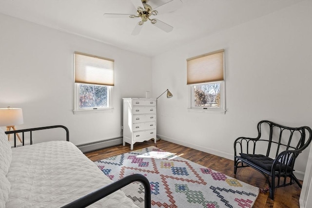 bedroom featuring a baseboard heating unit, multiple windows, wood finished floors, and baseboards