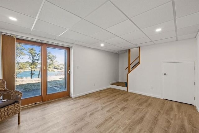 basement with light wood-style floors, stairs, baseboards, and a drop ceiling