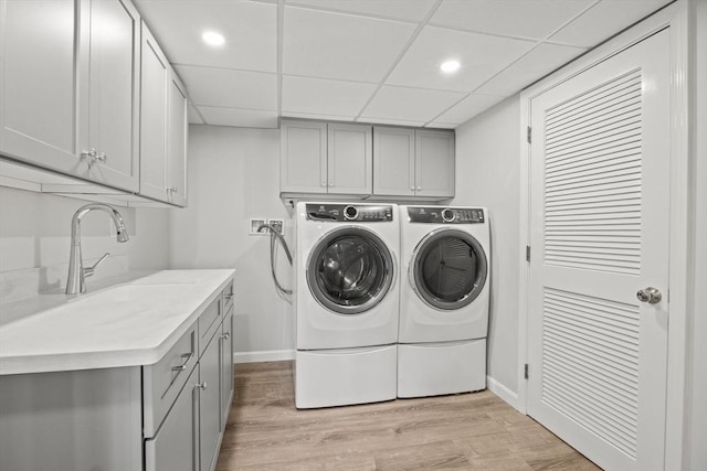 clothes washing area featuring cabinet space, baseboards, light wood-style flooring, washing machine and dryer, and a sink