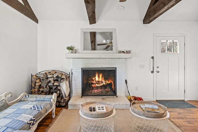 living area featuring beamed ceiling, a fireplace, wood finished floors, and a ceiling fan