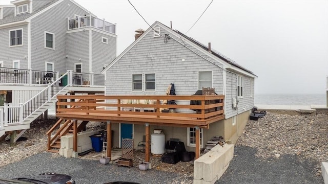 rear view of property with a chimney, a deck with water view, and stairway