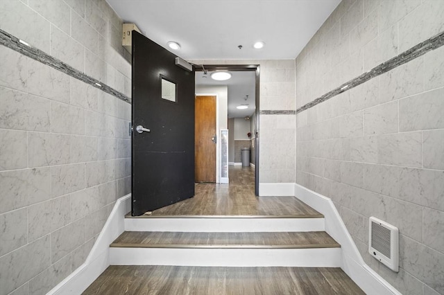 stairs featuring heating unit, wood-type flooring, and tile walls