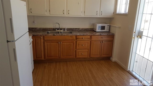 kitchen with dark stone counters, light hardwood / wood-style flooring, white appliances, and sink