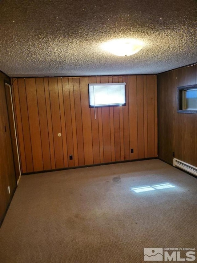 basement with wood walls, a textured ceiling, a baseboard radiator, and light colored carpet