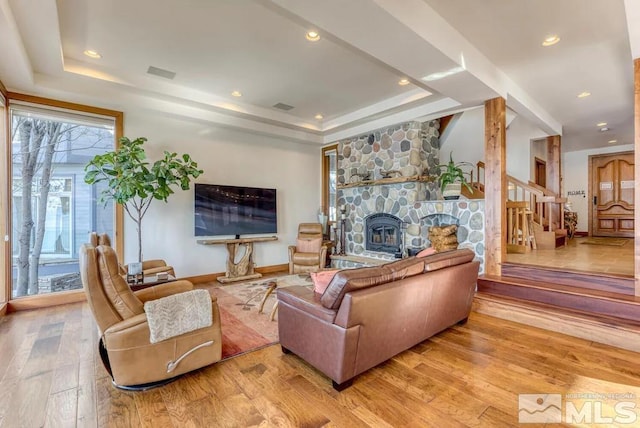 living room featuring a tray ceiling, a stone fireplace, light hardwood / wood-style flooring, and a wealth of natural light